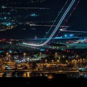 Vista aérea noturna de uma cidade com aeroporto e área portuária iluminados.