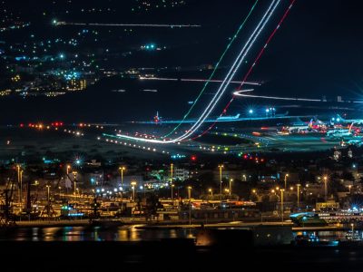 Vista aérea noturna de uma cidade com aeroporto e área portuária iluminados.
