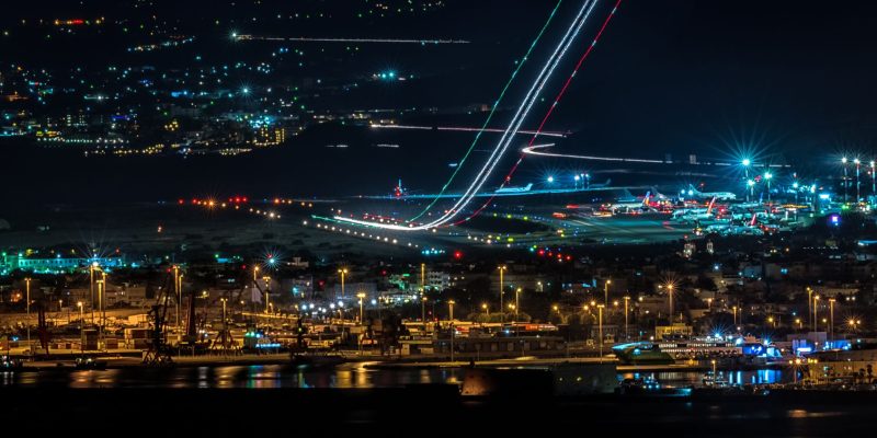 Vista aérea noturna de uma cidade com aeroporto e área portuária iluminados.
