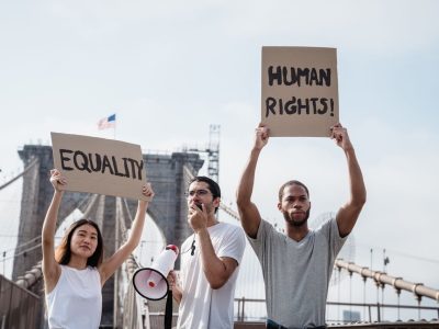Ativistas diversos seguram cartazes sobre igualdade e direitos humanos em uma ponte.
