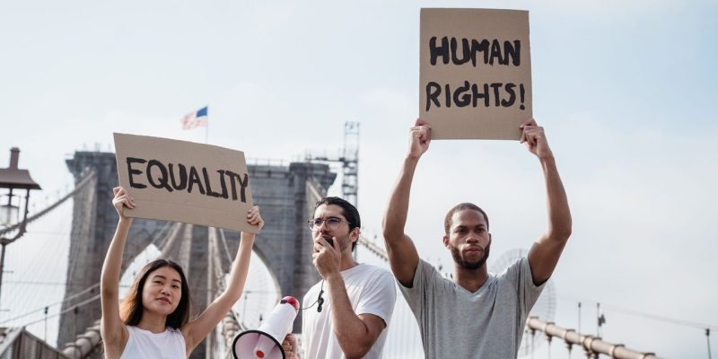 Ativistas diversos seguram cartazes sobre igualdade e direitos humanos em uma ponte.